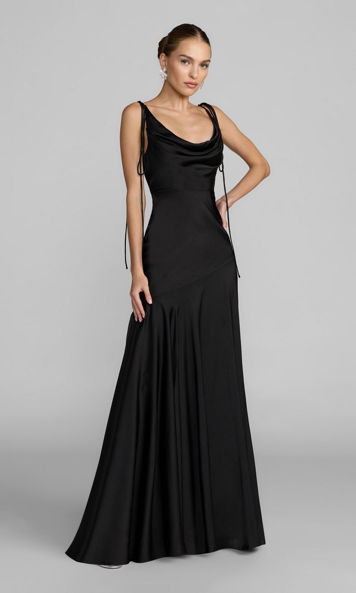 A woman stands against a plain gray background wearing the Mac Duggal 49914 long formal dress in black, featuring satin charmeuse fabric, a cowl neckline, tie shoulder straps, and a flared skirt.